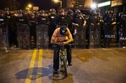 A man sits on a bicycle in front of a line of police officers in riot gear ahead of a 10 p.m. curfew in the wake of Mondays riots following the funeral for Freddie Gray, Tuesday, April 28, 2015, in Baltimore. (AP Photo/David Goldman)