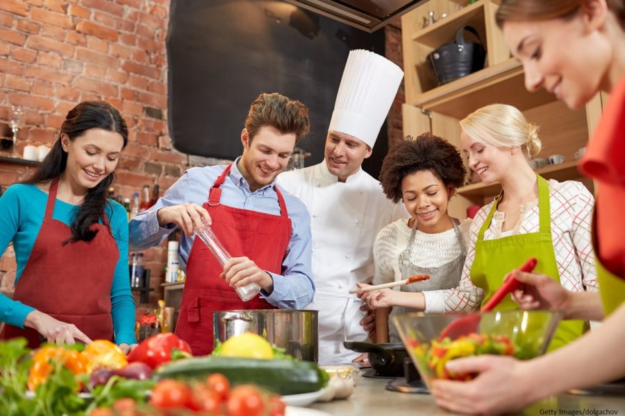 An instructor teaches a group of young adults how to cook.